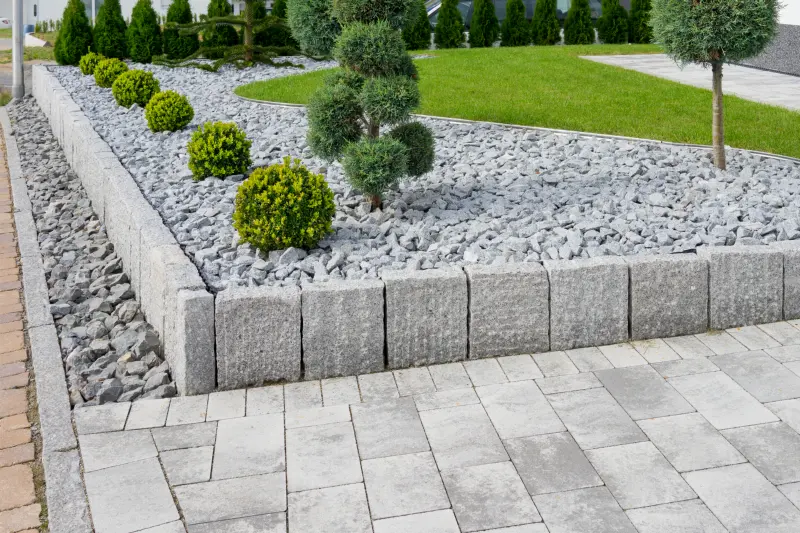 Abords d'une maison avec pavés, bordures en granit, massif de graviers et arbustes taillés