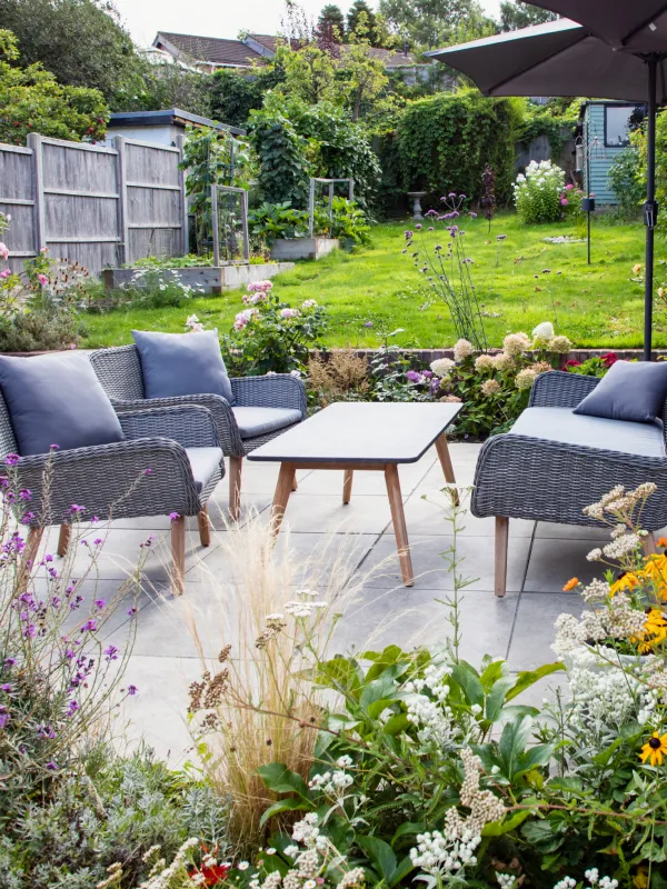 Jardin fleuri avec salon de jardin sur une terrasse dallée et pelouse en arrière-plan