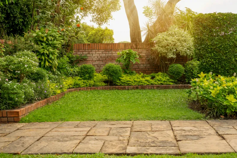 Jardin avec pelouse, massifs bordés de briques, arbustes taillés et allée en dalles