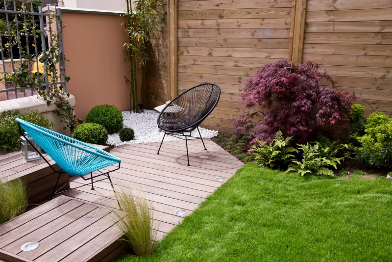Terrasse en bois avec deux fauteuils, spots encastrés et pelouse, devant une palissade en bois