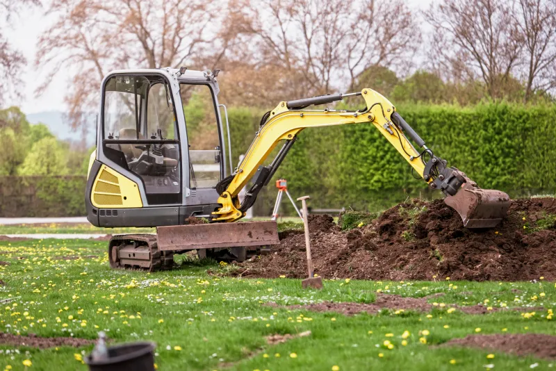 Mini-pelle en train de creuser et décaper le terrain d’un jardin
